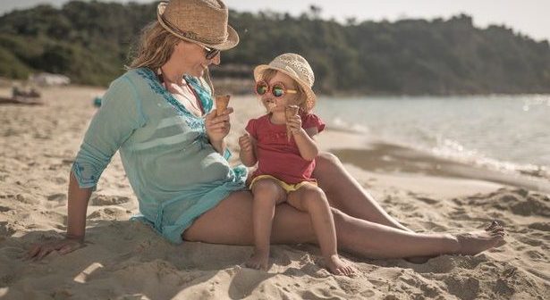 Mother with child on tropical beach on holiday eating ice cream