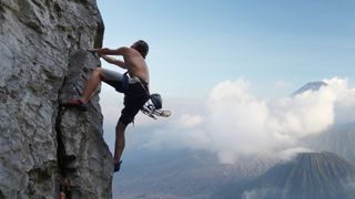 photo of a man rock climbing with mountains pictured in the background