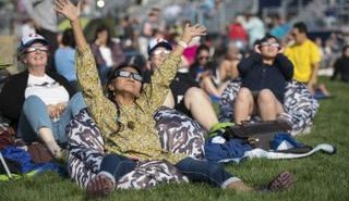 People wearing solar eclipse glasses sit in the grass to view the 2017 total solar eclipse over North America