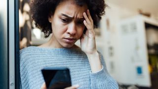 Woman looks anxiously at her phone with one hand on her forehead